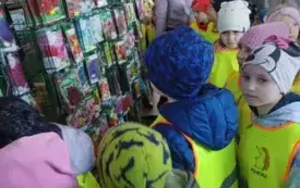 grupa dzieci w kamizelkach ochronnych stoi w sklepie ogrodniczym przed nimi saszetki z nasionami r&oacute;żnych kolorowych kwiat&oacute;w