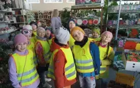 grupa dzieci w kamizelkach ochronnych stoi w sklepie ogrodniczym w tle kwiaty nasiona