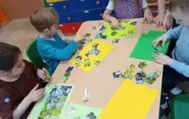 dzieci siedzą przy stoliku przed nimi puzzle