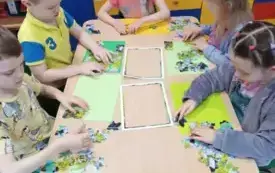 dzieci siedzą przy stoliku przed nimi puzzle