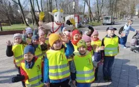 dzieci w kamizelkach odblaskowych pozuja do zdjęcia z postacią przebraną za koziołka matołka