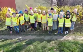 grupa dzieci w kamizelkach odblaskowych pozuje do zdjęcia na tle krzew&oacute;w forsycji
