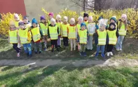 grupa dzieci w kamizelkach odblaskowych pozuje do zdjęcia na tle krzew&oacute;w forsycji