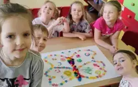 sz&oacute;stka dzieci wok&oacute;ł stolika na kt&oacute;rym leży praca plastyczna duży motyl ozdobiony r&oacute;żnymi kolorowymi elementami