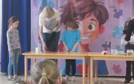 dwoje dzieci i pani przy stoliku w tle dekoracja związana z dniem świadomości autyzmu