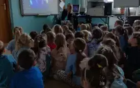 tablica multimedialna na niej prezentacja przed tablicą siedzą dzieci
