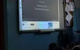 tablica multimedialna na niej prezentacja przed tablicą siedzą dzieci