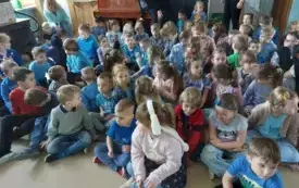 grupa dzieci w niebieskich strojach siedzi na dywanie