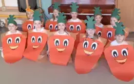grupa dzieci w przebraniach marchewki kuca na dywanie i pozuje do zdjęcia