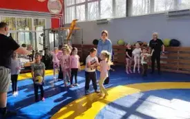 dzieci stoją w trzech rzędach z nimi panie i pan trener dwoje dzieci trzyma piłki do siatk&oacute;wki