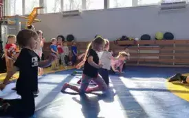 dzieci na macie do ćwiczeń w pozycji na kolanach w tle stoją pozostałe dzieci