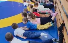 dzieci wraz z panem trenerem leżą na macie obok siebie w pozycji uniesionej głowy i n&oacute;g
