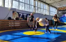 na macie do ćwiczeń dw&oacute;ch chłopc&oacute;w w parze a pomiędzy nimi duża piłka gimnastyczna obok nich pan i pani pani robi zdjęcia
