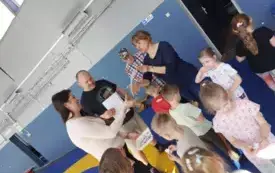 grupa dzieci wśr&oacute;d nich dwie panie i dw&oacute;ch pan&oacute;w jeden z pan&oacute;w dużo starszy, pani nauczycielka wręcza podziękowanie na piśmie pani kt&oacute;ra pomogła zorganizować zajęcia
