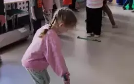 dziewczynka stoi w obręczy  druga obręcz leży przed nią dziewczynka trzyma w niej drążek widać inne dzieci na sali