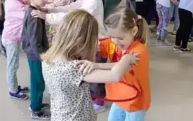 dzieci na sali stoją w parach trzymają sie za ramiona pomiędzy nimi obręcze