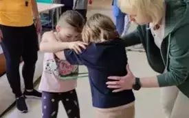 dwoje dzieci stoi w parze trzymają sie za ramiona pomiędzy nimi obręcz obok panie nauczycielki