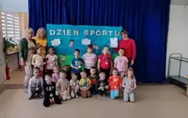 dzieci i trzy nauczycielki pozują do zdjęcia na tle dekoracji z napisem dzień sportu dzieci maja na szyjach medale pani nauczycielka trzyma dyplom