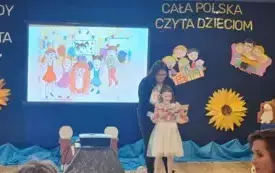 dziewczynka trzyma otworzoną książkę za nią pani nauczycielka w tle napi cała polska czyta dzieciom oraz obrazki dzieci