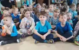 grupa dzieci w niebieskich ubraniach siedzi na dywanie
