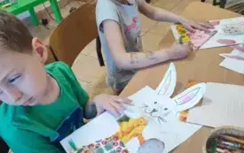 dwoje dzieci przy stoliku wykonują prace plastyczne zajączki