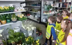 grupa dzieci w kamizelkach odblaskowych stoi przed regałęm z akcesoriami i ozdobami do ogrodu