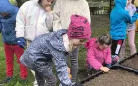 dzieci stoją przy skrzyniach z ziemią dziewczynka trzyma w szpadelek w ziemi 