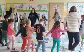 dzieci stoją w kole na dywanie trzymając się za ręce z nimi cztery panie 