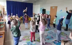 dzieci i dwie panie nauczycielki stoją na dywanie i trzymają w g&oacute;rze w dłoniach jajko (każdy)