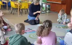 dzieci siedzą na dywanie przed nimi pani nauczycielka kt&oacute;ra trzyma w dłoni jajko