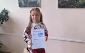 dziewczynka z dyplomem i torebką prezentową pozuje do zdjęcia w tle na ścianie zdjęcia kwiat&oacute;w