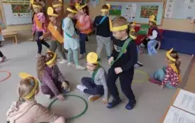 dzieci w opaskach i szarfach w r&oacute;żnych kolorach stoją na dywanie lub siedzą przy obręczy