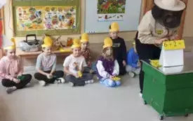 dzieci w opaskach na głowach siedzą pod ścianą pani nauczycielka w stroju pszczelarza prezentuje przykład na dodawanie
