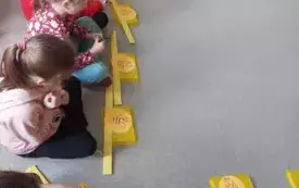 dzieci siedzą na dywanie przed nimi opaski w koorze ż&oacute;łtym a na nich rysunki pszcz&oacute;ł