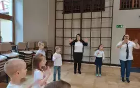 dzieci i panie stoją w kole z rękami uniesionymi w g&oacute;rę