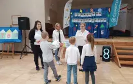 troje dzieci stoi przed paniami jedna z nich wręcza im dyplom w tle dekoracja olimpiada matematyczna