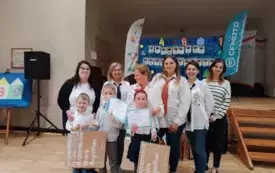 troje dzieci i sześć pań w galowych strojach pozują do zdjęcia w tle dekoracja z napisem olimpiada matematyczna