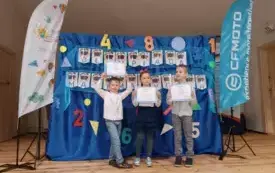 troje dzieci z dyplomami w rękach stoi na tle dekoracji z napiecem olimpiada matematyczna