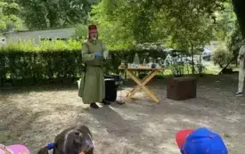 pan alchemik stoi przy stoliku z akcesoriami alchemicznymi z przodu stoją dzieci