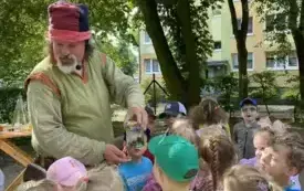 pan alchemik stoi wśr&oacute;d dzieci i trzyma słoik z czymś w środku