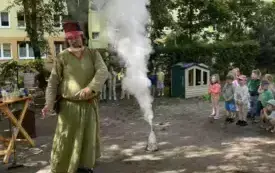 pan alchemik stoi przy naczyniu kt&oacute;re mocno dymi obok stoi grupka dzieci