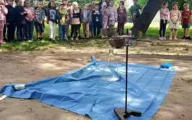 niebieska płachta rozłożona na ziemi na niej akcesoria alchemiczne w tle duża grupa dzieci