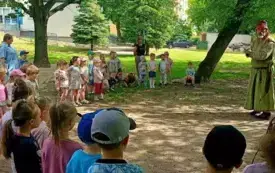 pan alchemik w centrum dzieci stoją dookoła z nimi panie nauczycielki