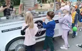 dzieci stoją przy w&oacute;zku z lodami pan i pani wydają lody