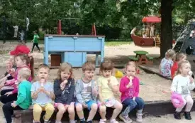 dzieci z młodszej grupy siedzą na brzegu piaskownicy i jedzą lody