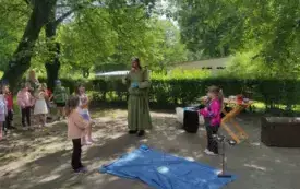 pan alchemik w centrum obok niego trzy dziewczynki dalej stoją dzieci z grup na środku leży niebieska płachta i stoją narzędzia alchemiczne
