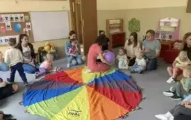 pani nauczycielka siedzi z balonem w rękach i m&oacute;wi coś do rodzic&oacute;w i dzieci siedzących wok&oacute;ł