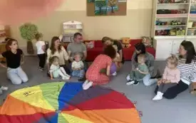 pani nauczycielka siedzi z balonem w rękach i m&oacute;wi coś do rodzic&oacute;w i dzieci siedzących wok&oacute;ł