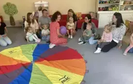 pani nauczycielka siedzi z balonem w rękach i m&oacute;wi coś do rodzic&oacute;w i dzieci siedzących wok&oacute;ł