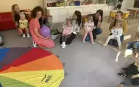 pani nauczycielka siedzi z balonem w rękach i m&oacute;wi coś do rodzic&oacute;w i dzieci siedzących wok&oacute;ł